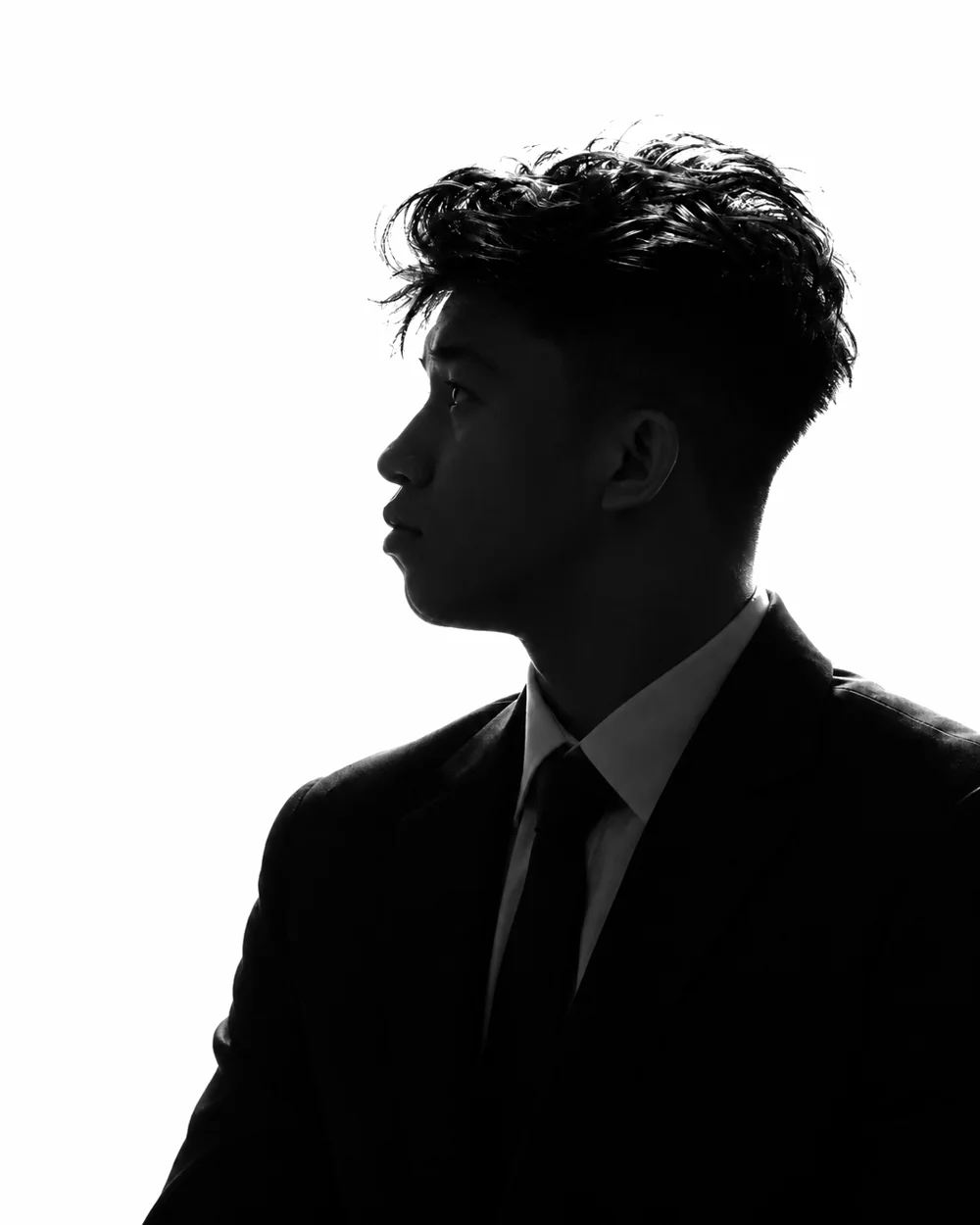 Jhon Wilfred Drio in a suit, backlit, looking up to the left